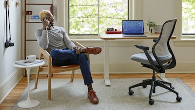A professional talking on a cell phone in their home office, featuring a ReGeneration Chair and Hipso Height-Adjustable Desk.