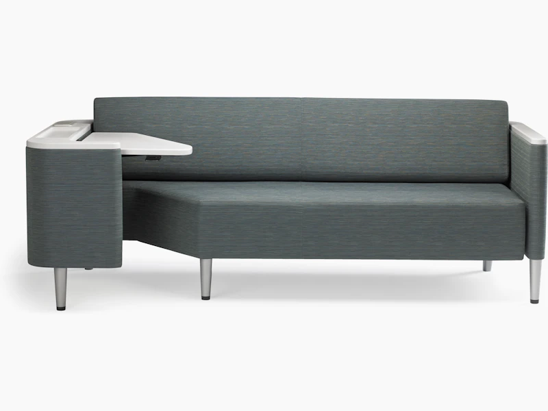 A Palisade Flop sofa in dark grey textile with white solid surface arms caps and white adjustable table with Durawrap top.