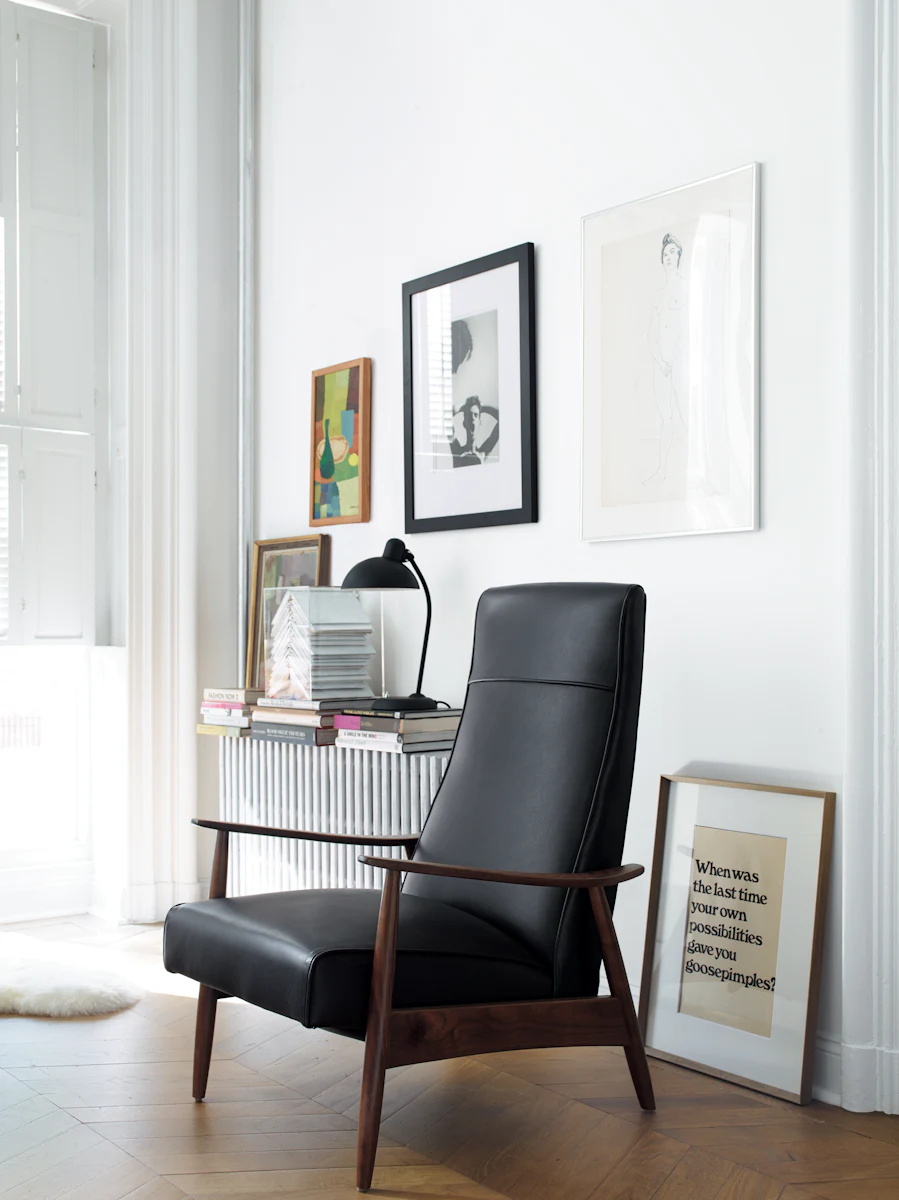 Home office/study area with a white wall, gallery frames, and a black leather chair; several books and decor items.