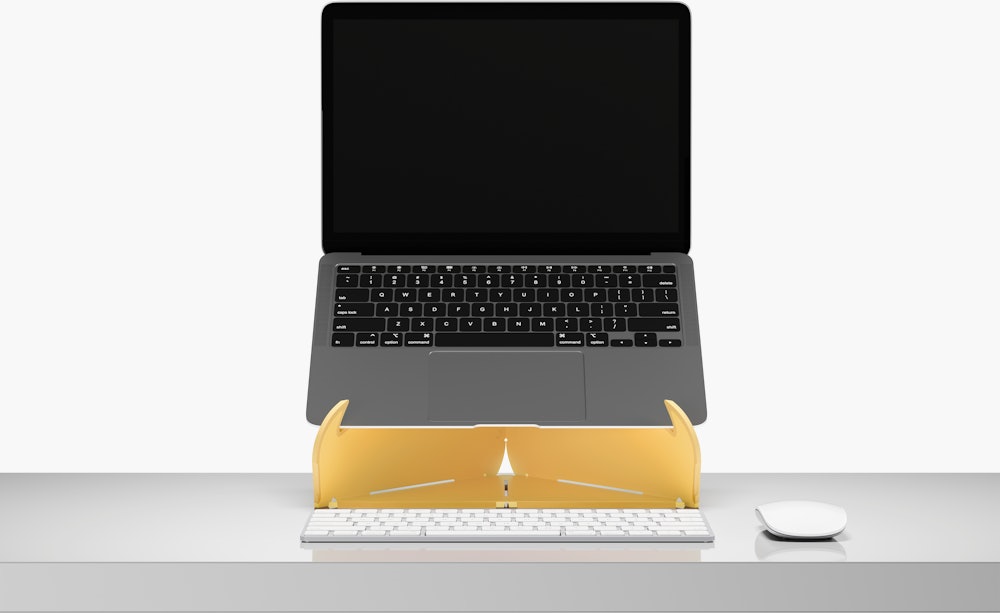 An open laptop raised to eye level on an Oripura Laptop Stand In yellow placed on a desk with work tools.