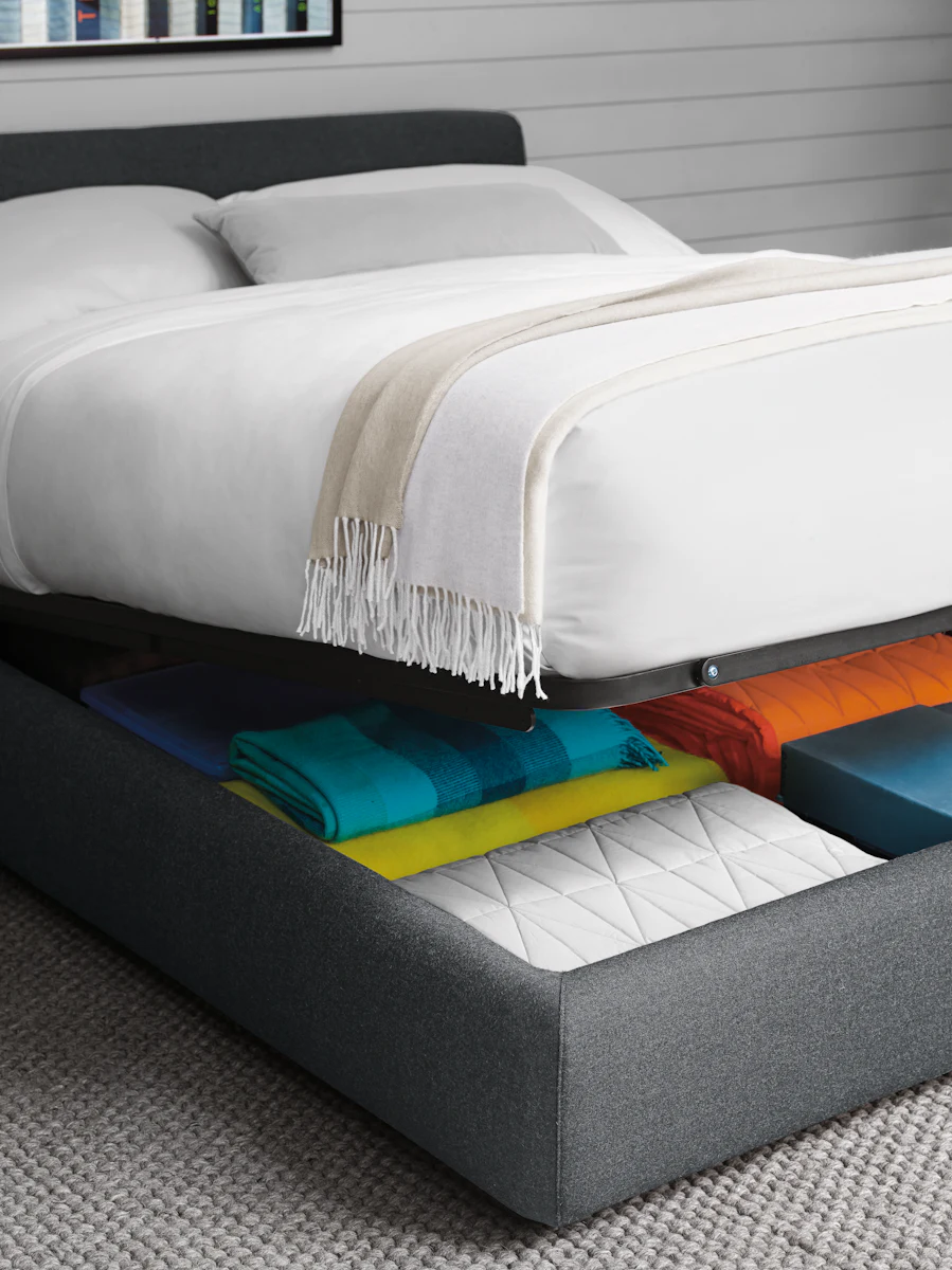 Bedroom with bed whose mattress is lifted to reveal storage underbed drawers