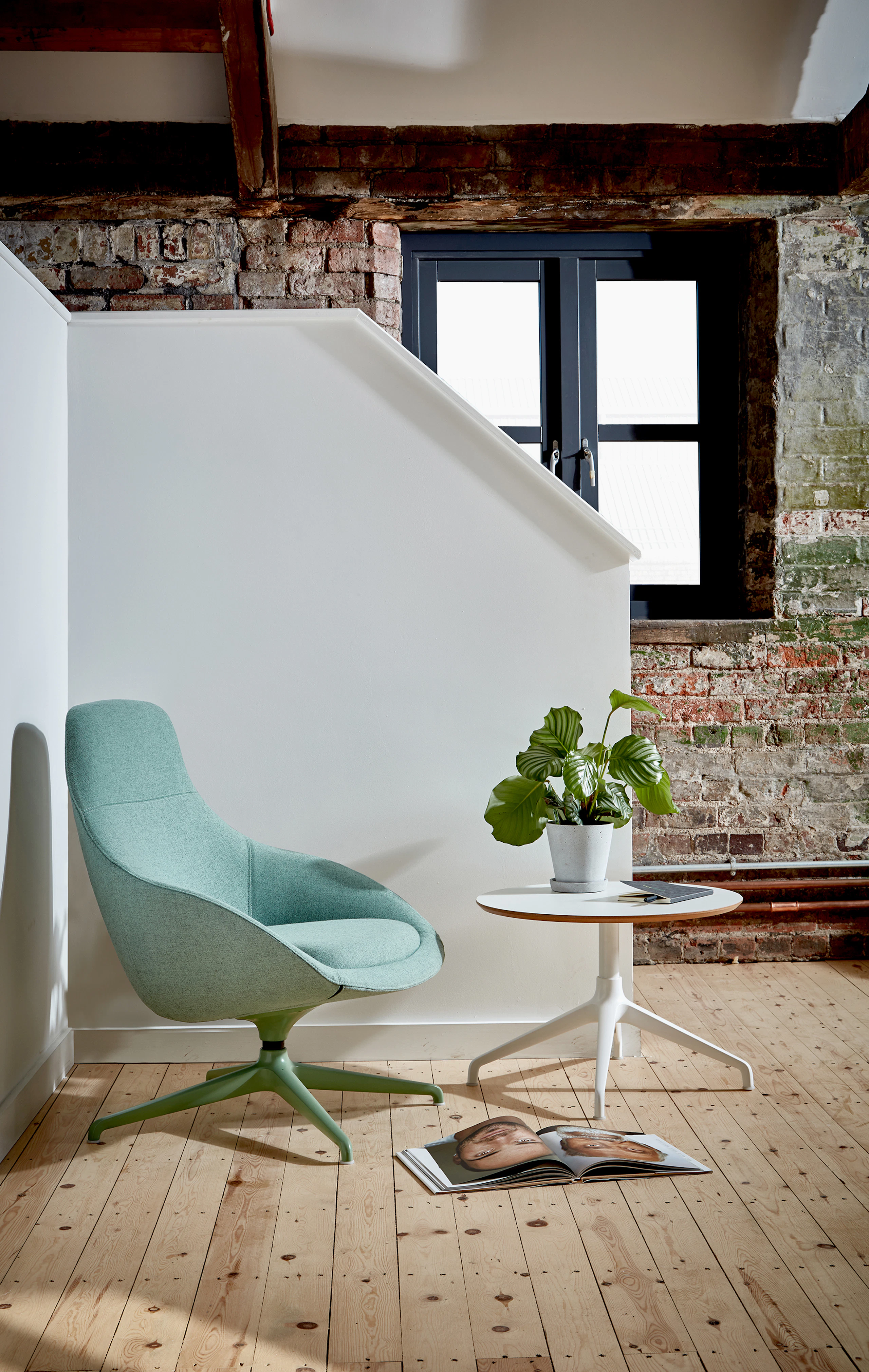 A green upholstered Always Lounge Chair fitted with a coordinating 4-star swivel base beside a white Ali Table, both from naughtone.