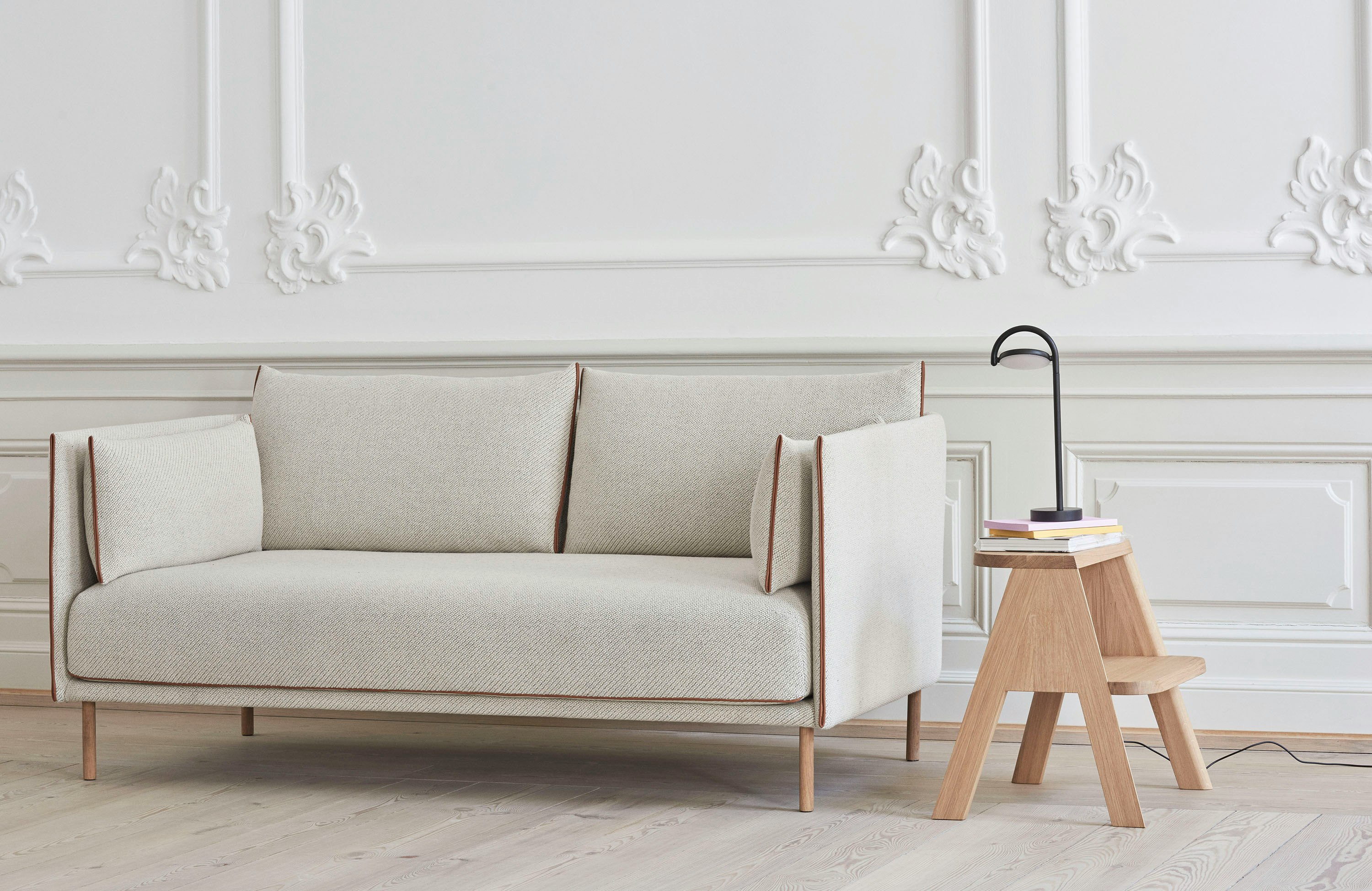 A Butler Step Stool with a black Marselis Table Lamp on top next to a Silhouette Sofa.