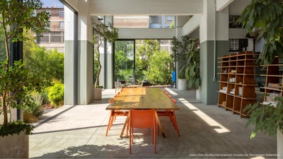 A meeting space in the interior of the JSa office filled with lush green plants, bookshelves, and floor-to-ceiling windows