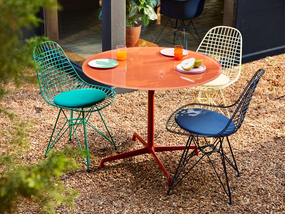 Herman Miller x  HAY, outdoor setting of green, black blue, and yellow Wire chairs and iron red Eames table