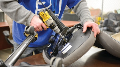 A close-up view of a person holding the base, underside, section of an office chair and using a drill to secure parts during assembly.