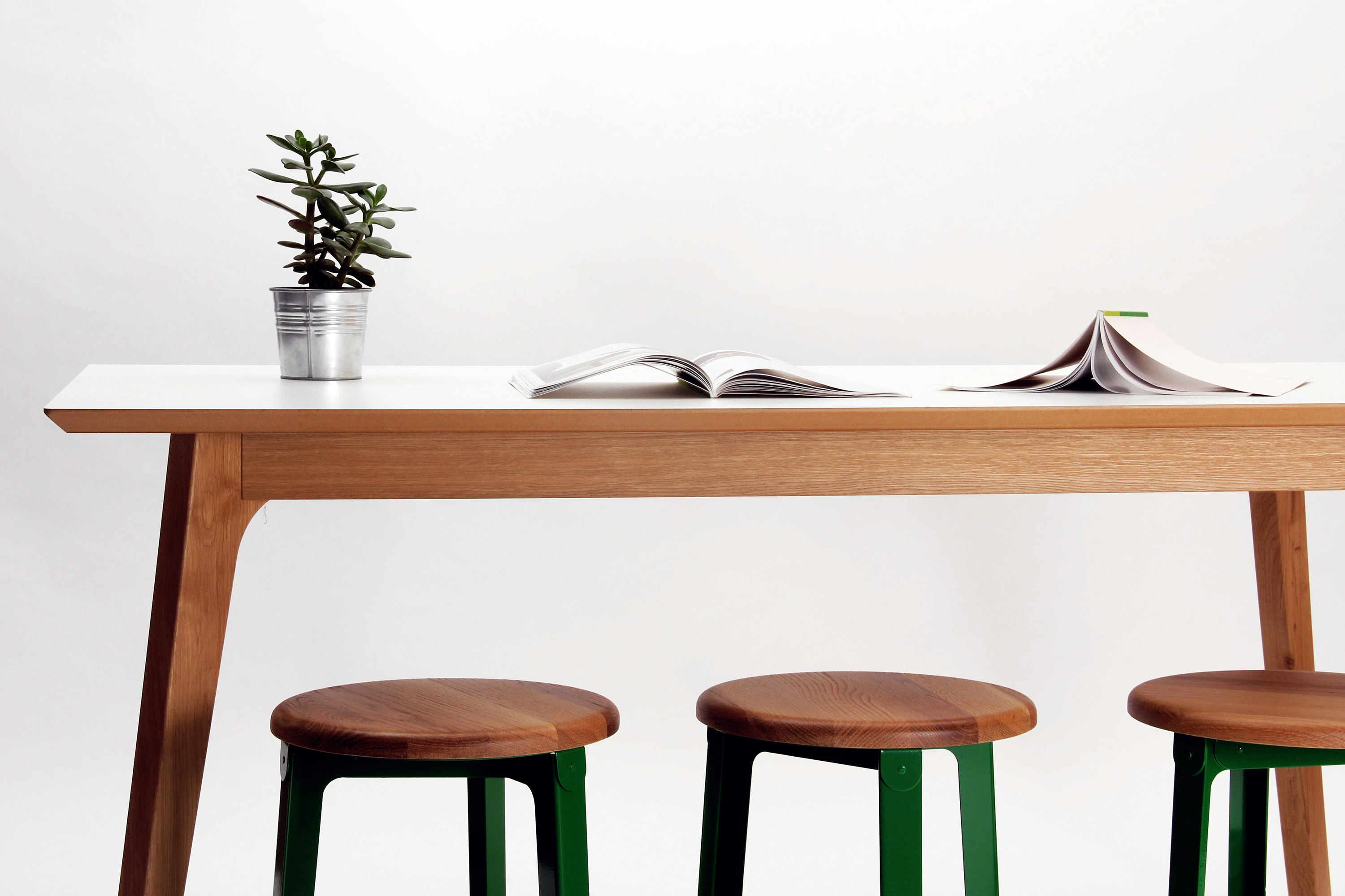 A Dalby Bar-Height Table with wood legs and a white table top, next to three bar-height Construct Stools.