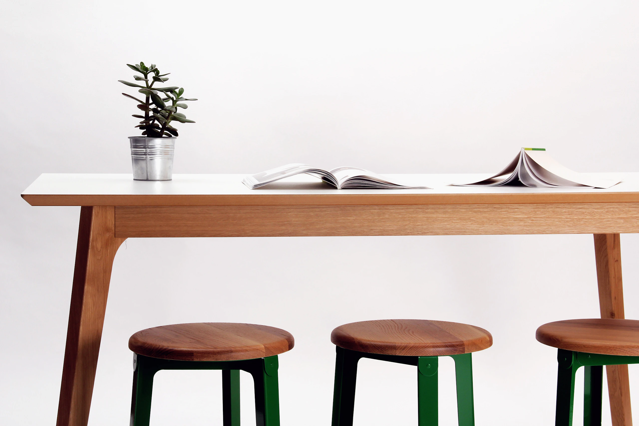 A Dalby Bar-Height Table with wood legs and a white table top, next to three bar-height Construct Stools.