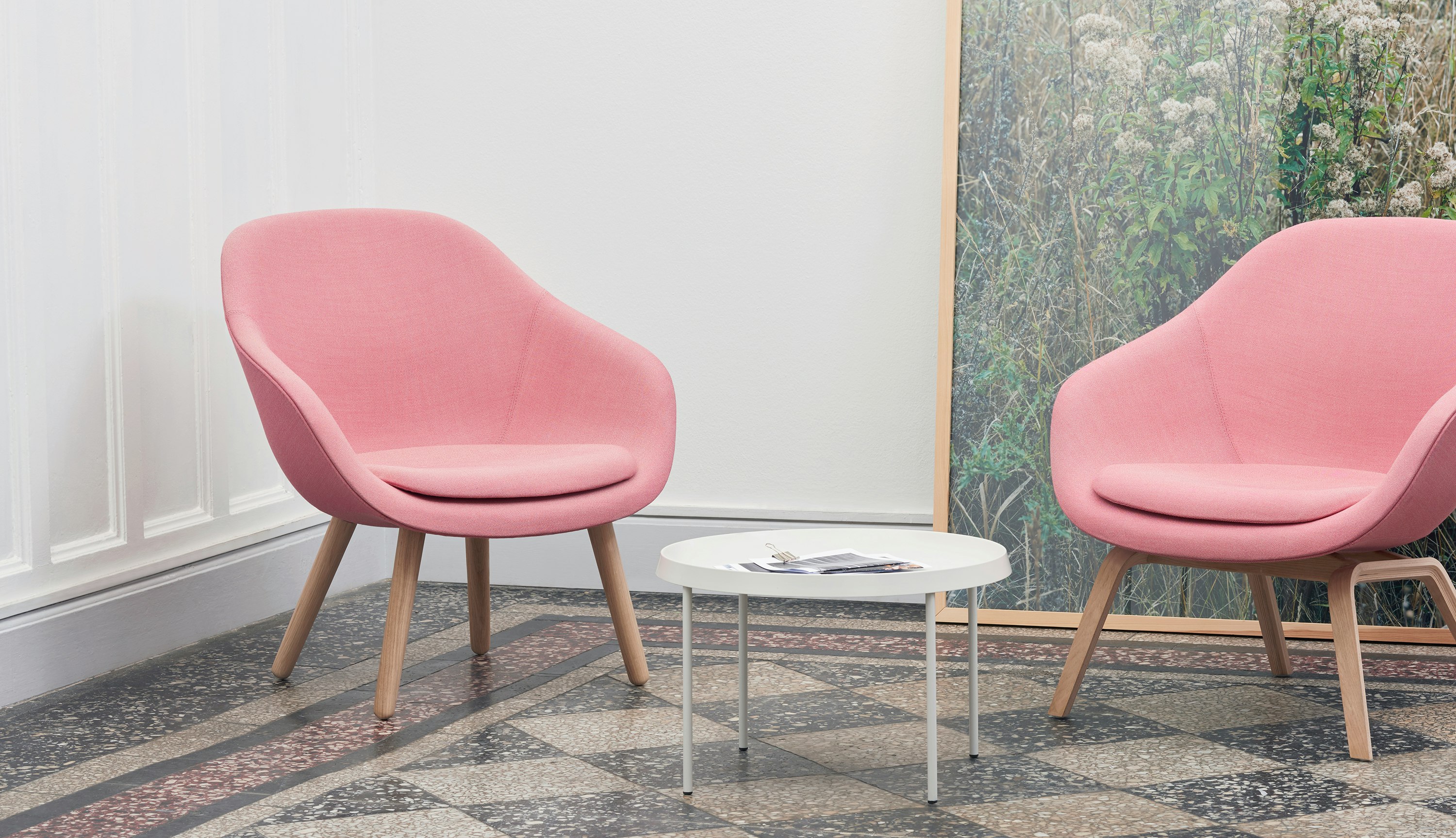 Two pink About A Lounge Chairs with wooden bases, and a Tulou Coffee Table in white.