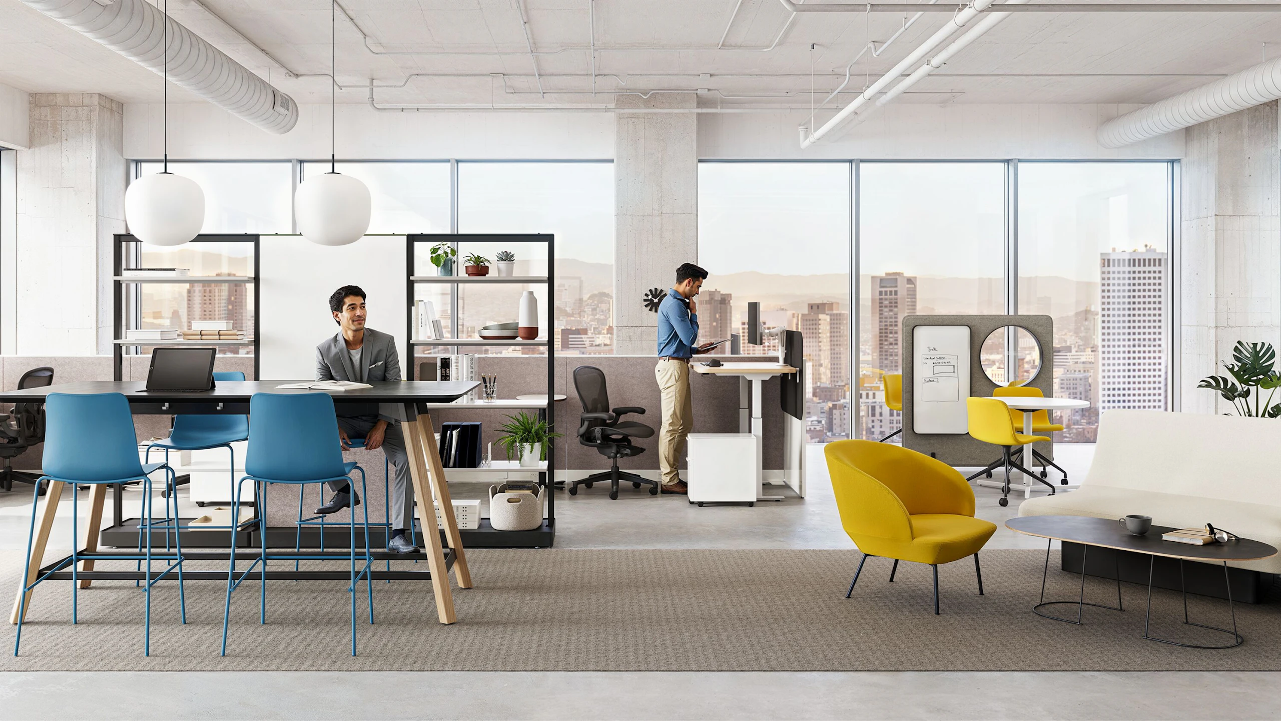 Two individuals working in a group office setting furnished with Herman Miller Passport Work Tables, NaughtOne Rhyme and Muuto Oslo Lounge boost chairs, and Herman Miller OE1 and NaughtOne Morse Bar Tables