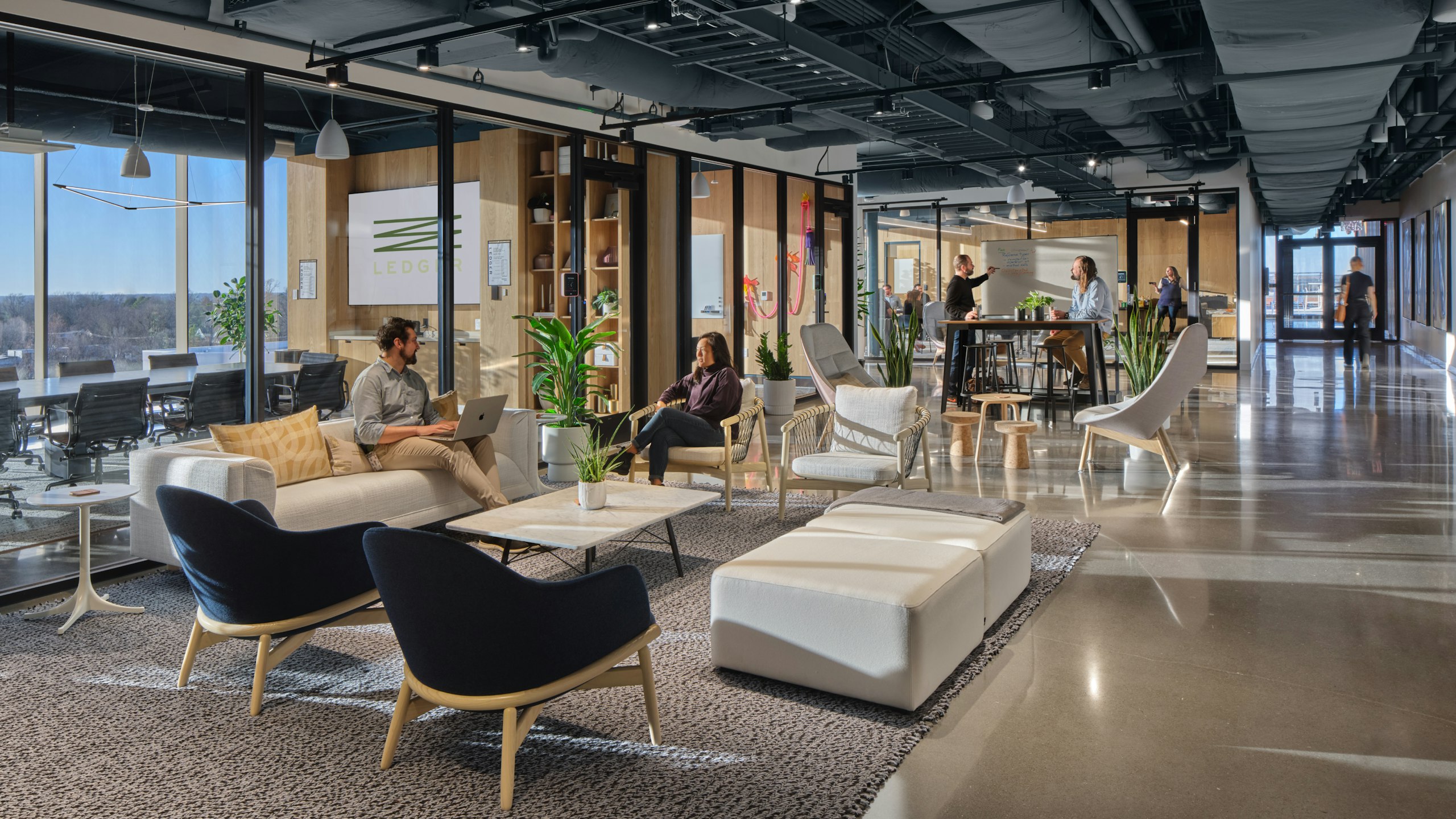 Groups of individuals having discussions in a communal office space furnished with Uchiwa Lounge Chairs by Hay