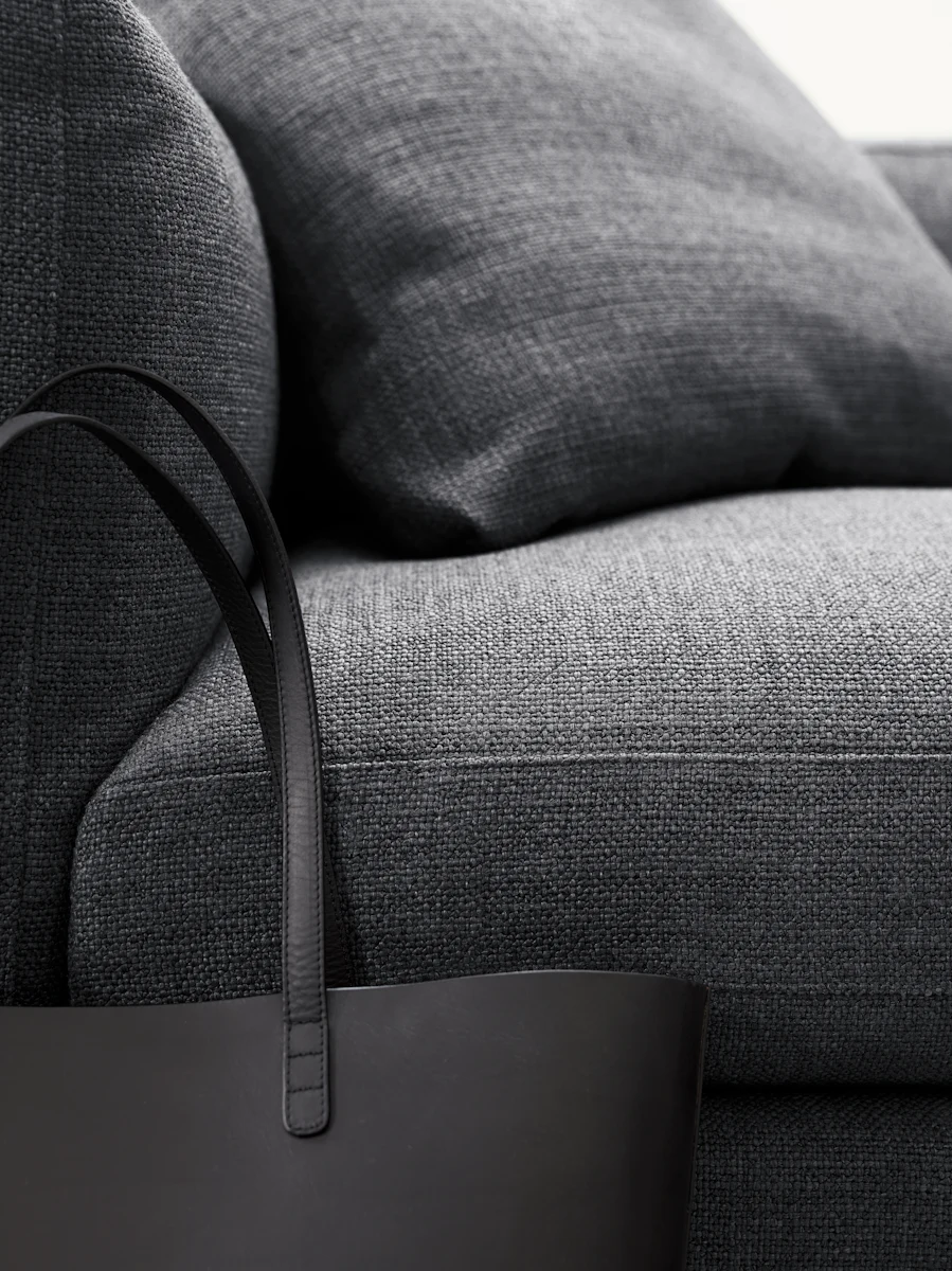Dark gray fabric sofa with cushions and a tote bag on a sofa edge