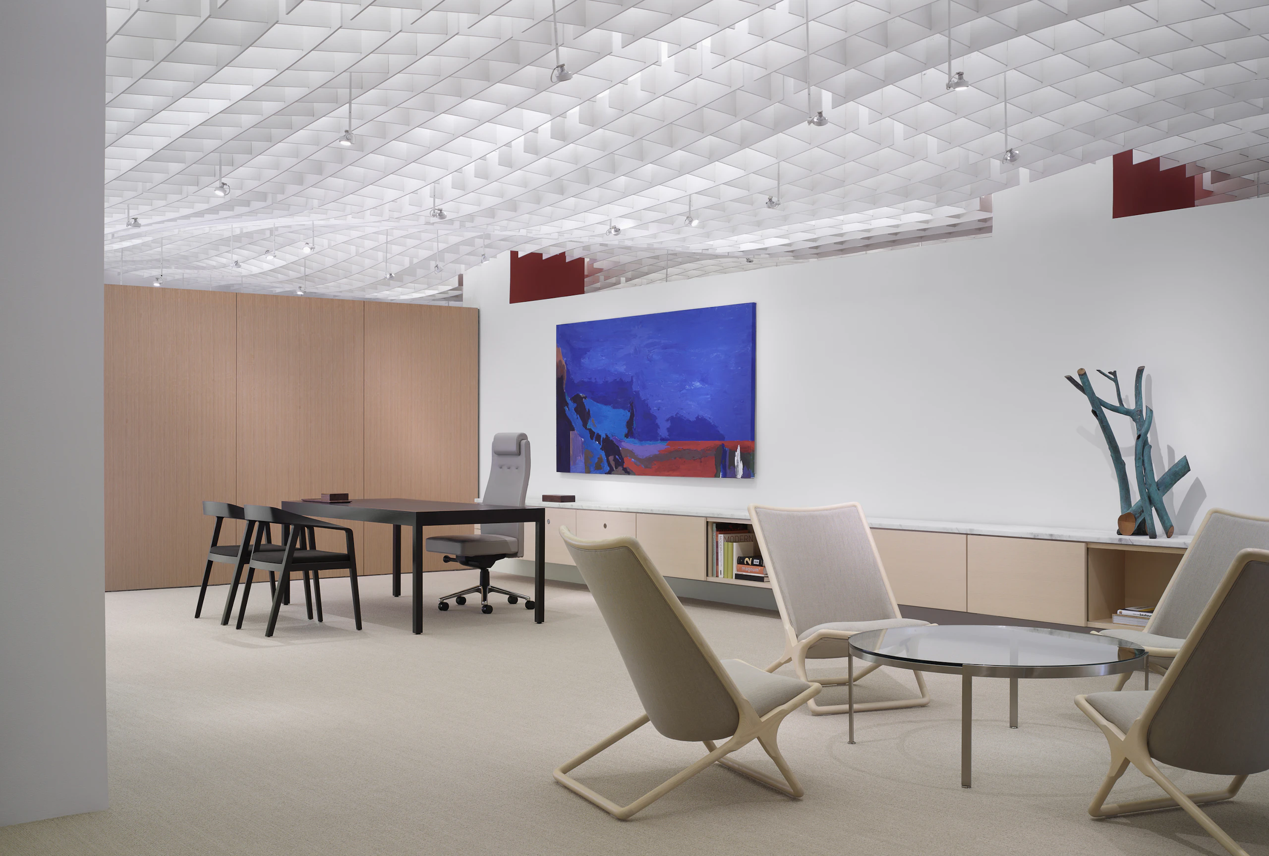 An executive suite featuring a desk in the background and a round Metal Series coffee table surrounded by four beige Scissor Chairs in the foreground.