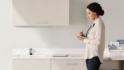Exam room wall of Mora casework in a light wood laminate finish and a physician standing and taking notes.
