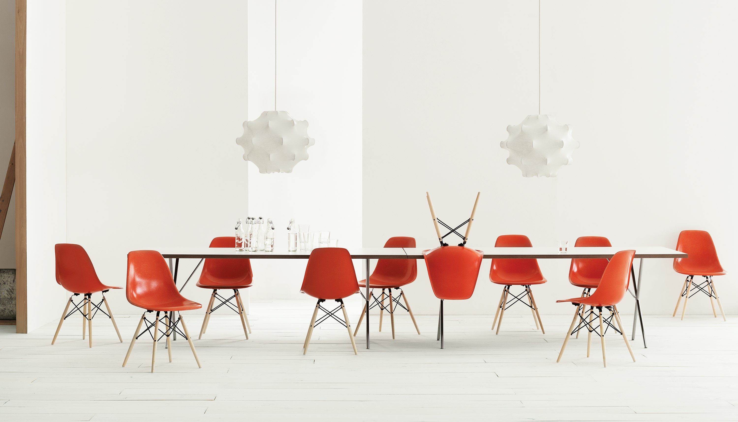 A setting of Eames Molded Fiberglass Side Chairs in Red Orange with Maple Dowel Legs and Nelson X-Leg Table.
