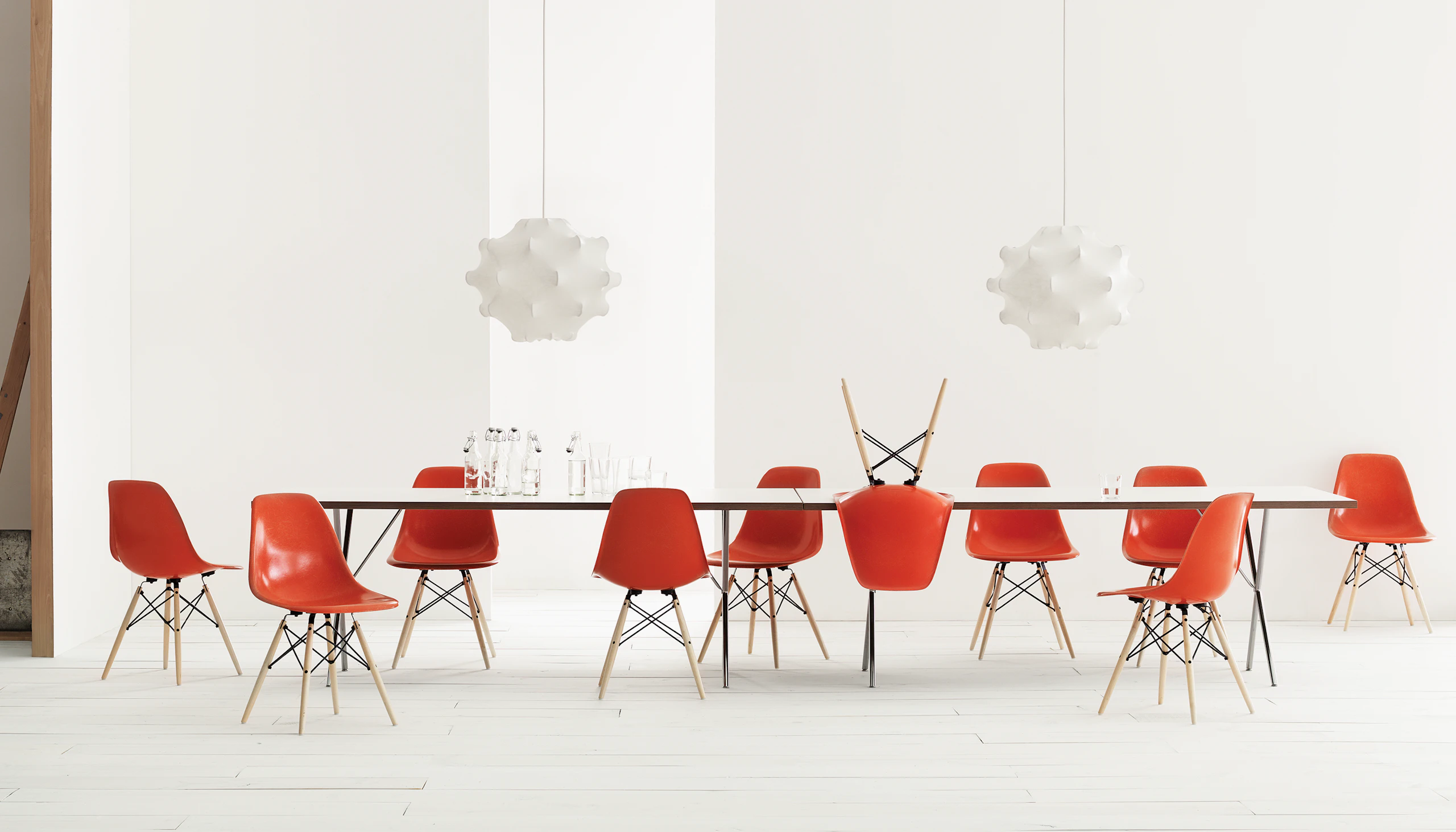 A setting of Eames Molded Fiberglass Side Chairs in Red Orange with Maple Dowel Legs and Nelson X-Leg Table.