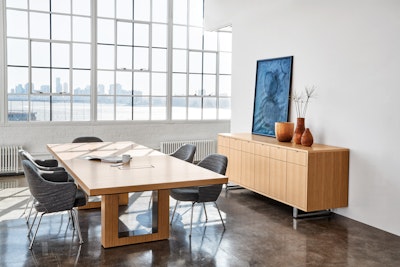 A large wood conference table surrounded by grey chairs with a light wood storage cabinet in the background.