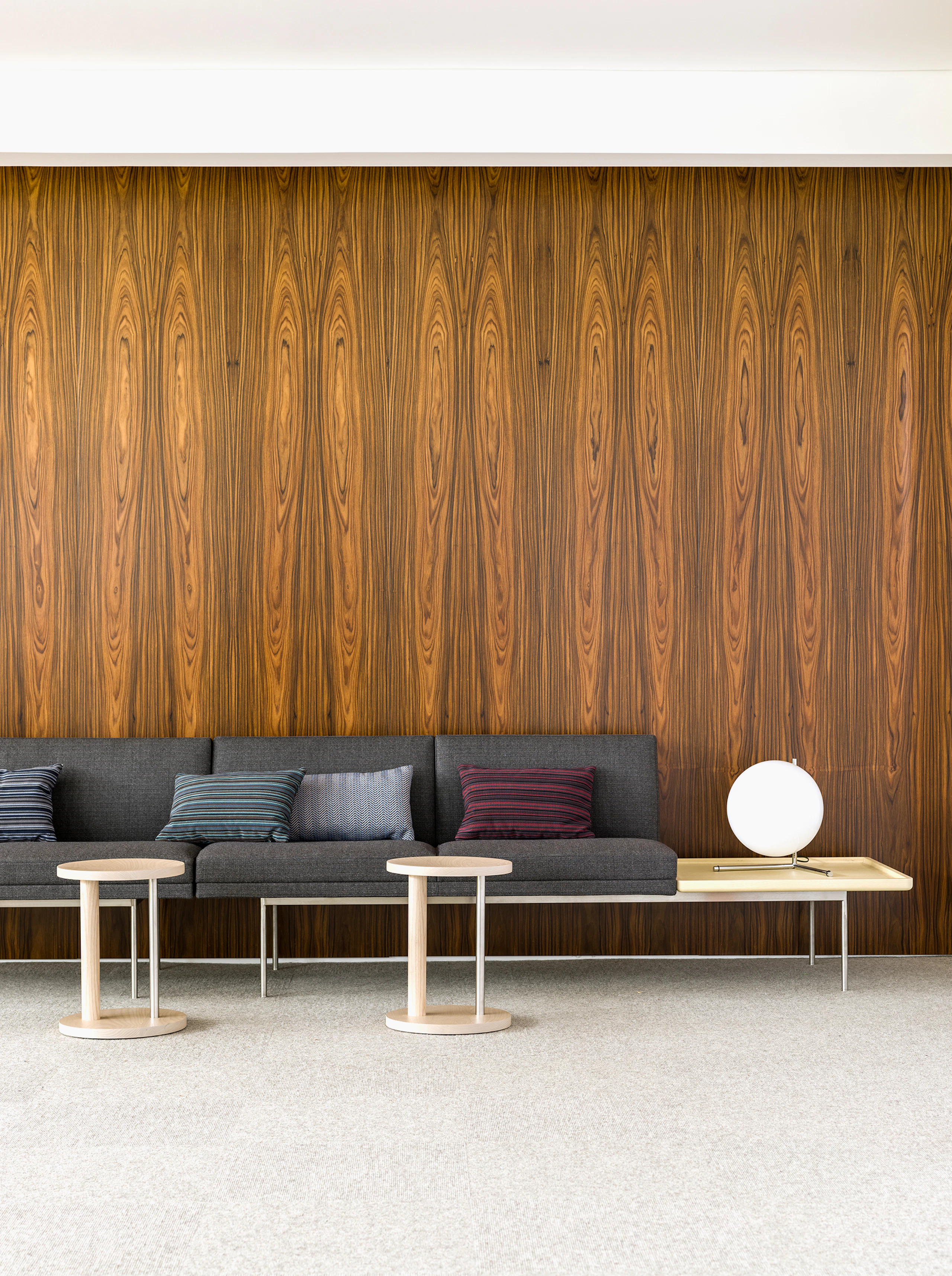 Partial view of a lounge space featuring a dark gray Tuxedo Component settee with an attached table and accent pillows.