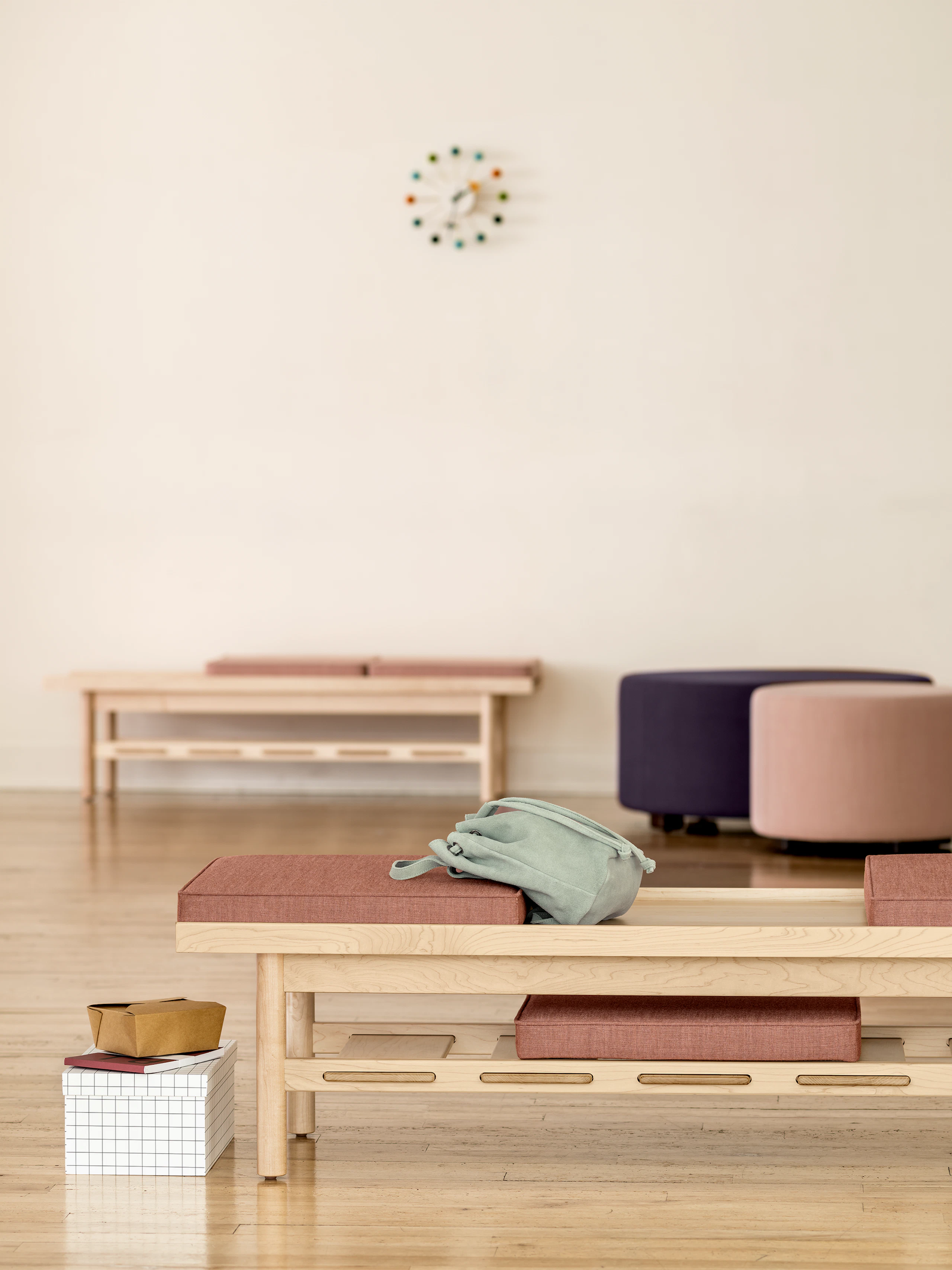 Two Nemschoff Tamarack Table and Benches in an ash finish with one in the foreground and one in the background and two Nemschoff Steps Ottomans nearby.
