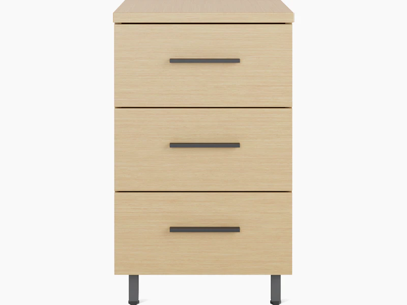 Front view of a single Nemschoff Bedside Cabinet in a oak on ash finish with three drawers, graphite bar pulls, and metal raised legs.