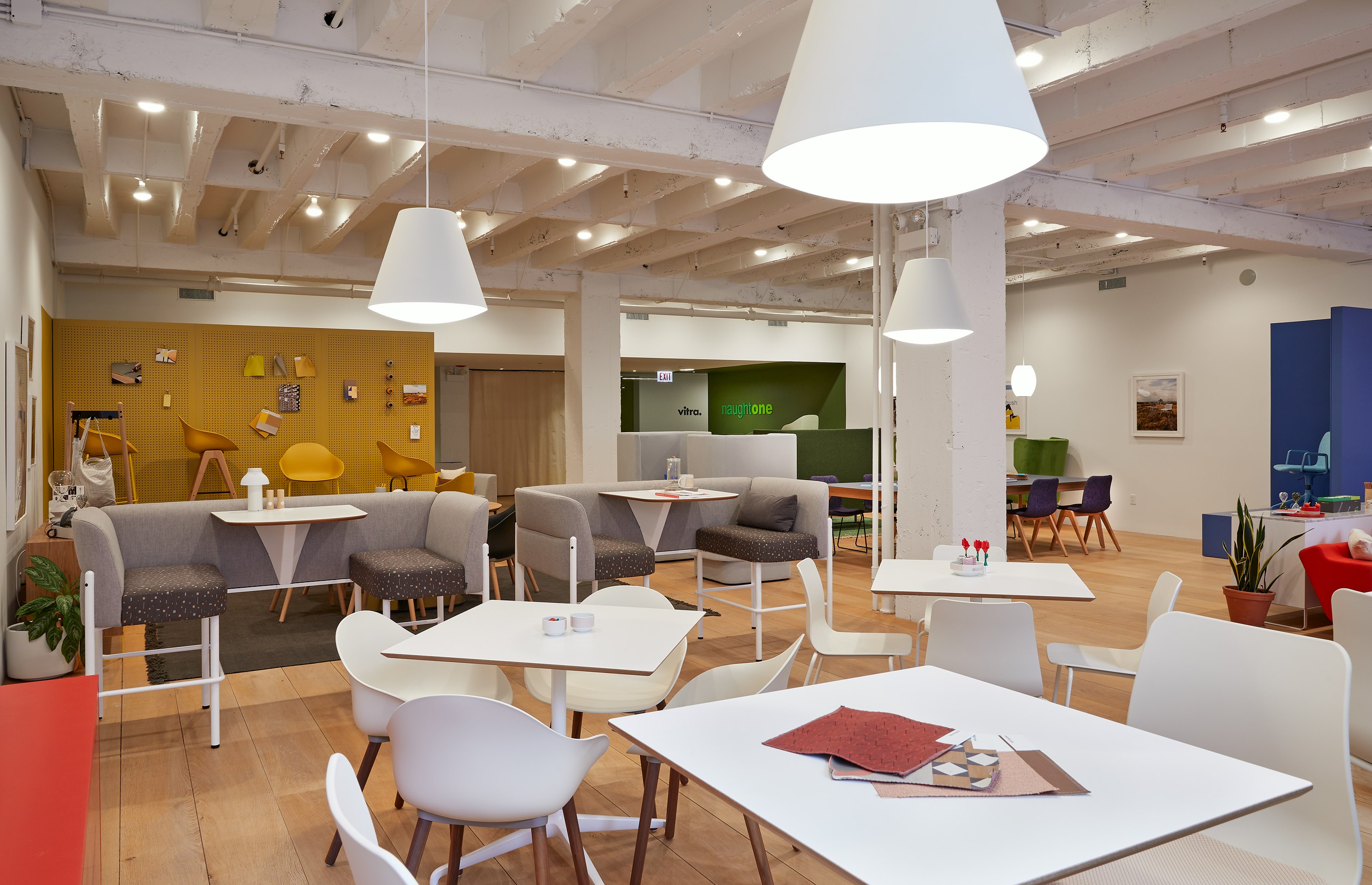 A cafe scene with white Polly and Ruby chairs around Ali Cafe Tables, and bar height Hue booths.