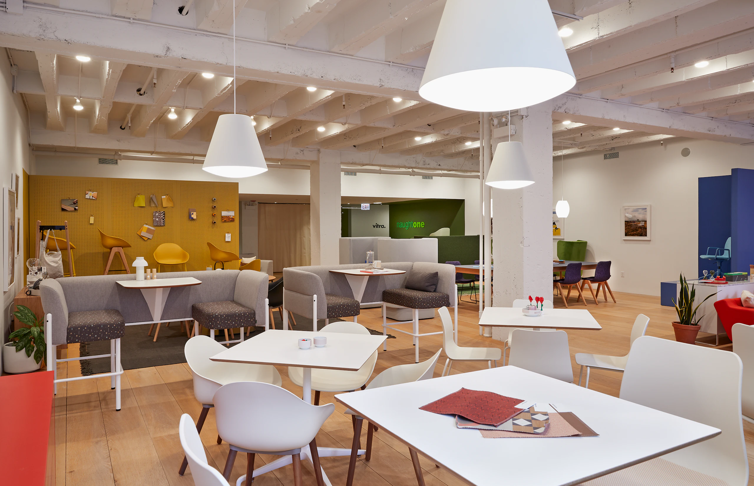 A cafe scene with white Polly and Ruby chairs around Ali Cafe Tables, and bar height Hue booths.