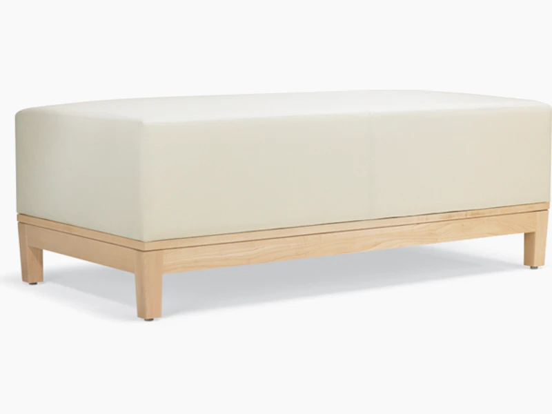 A three-quarter view of a Brava Platform Lounge Bench with maple base and white textile.