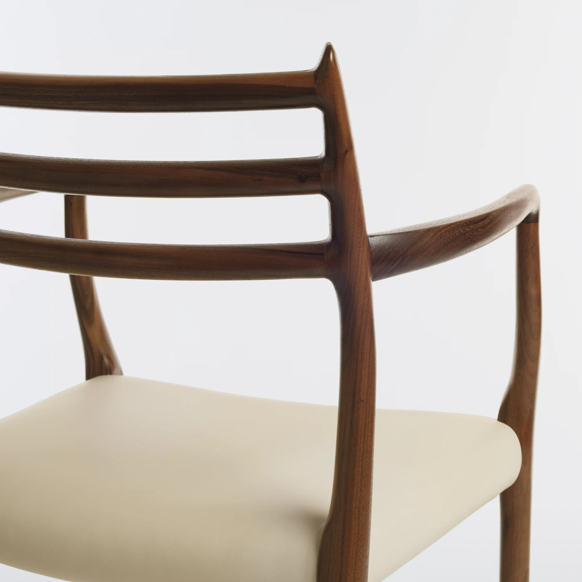 Moller Model 62 armchair detail showing walnut frame and cream leather seat.