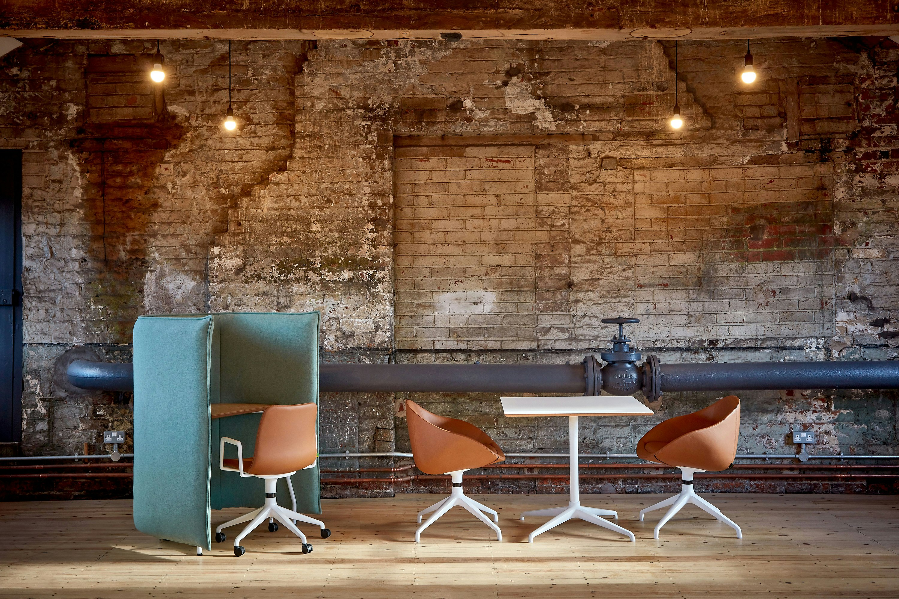 A leather upholstered Polly Chair with a 5-star white base and armrests placed at a pale green Cloud 1.5 desk with a brick background wall.