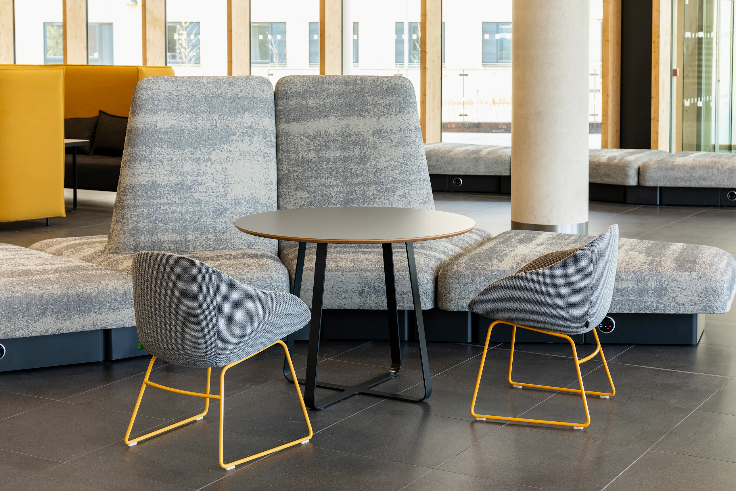 A gray patterned naughtone Rhyme Modular Seating unit paired with a black Frog Café Table and two gray patterned Always Chairs with yellow sled bases.