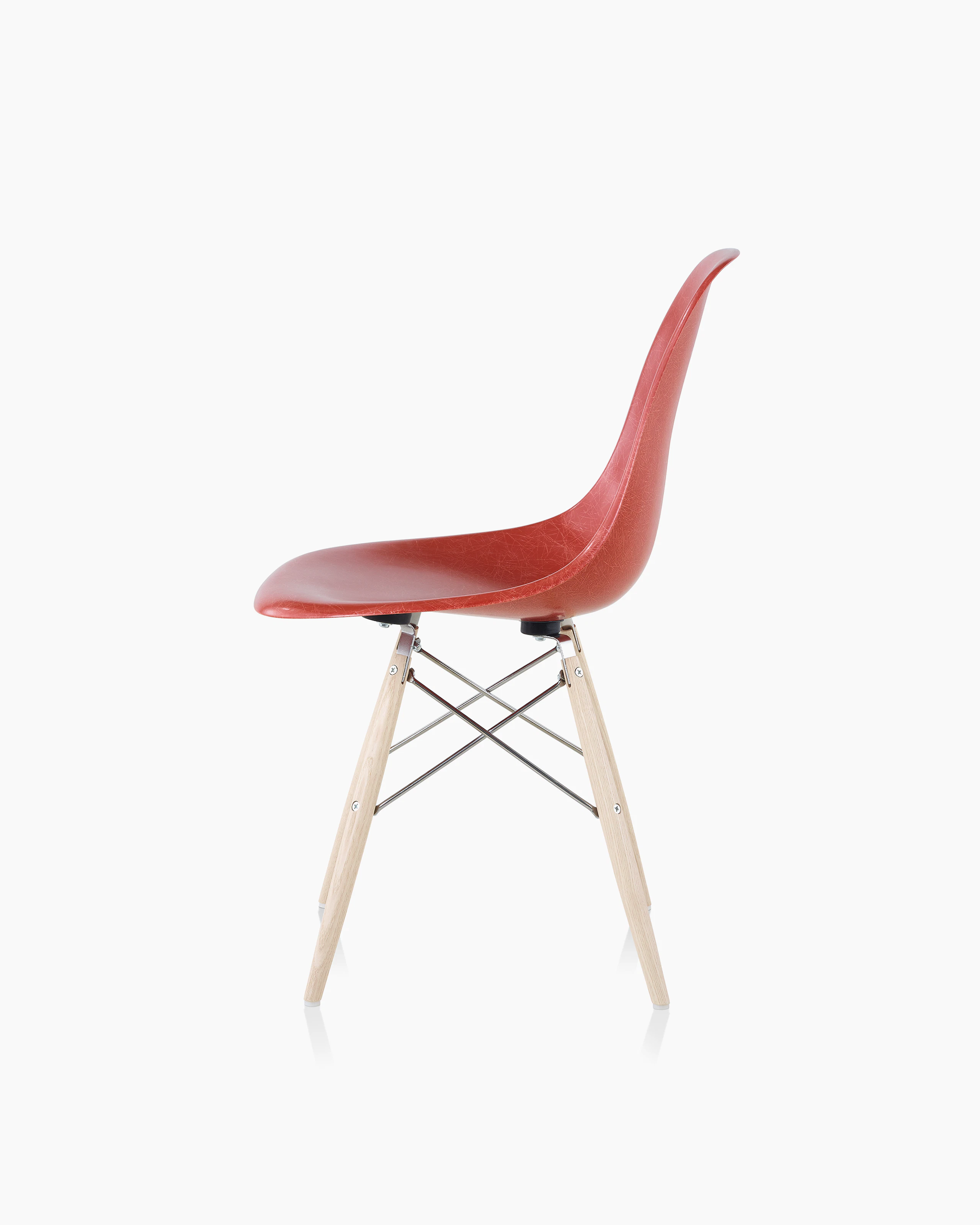 An Eames Molded Fibrglass Side Chair with a dowel base and red seat, viewed from the side.