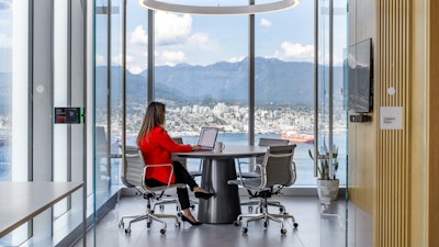 A person in a red jacket sitting in an Eames aluminum group chair in the Capilano meeting room at Blakes law firm