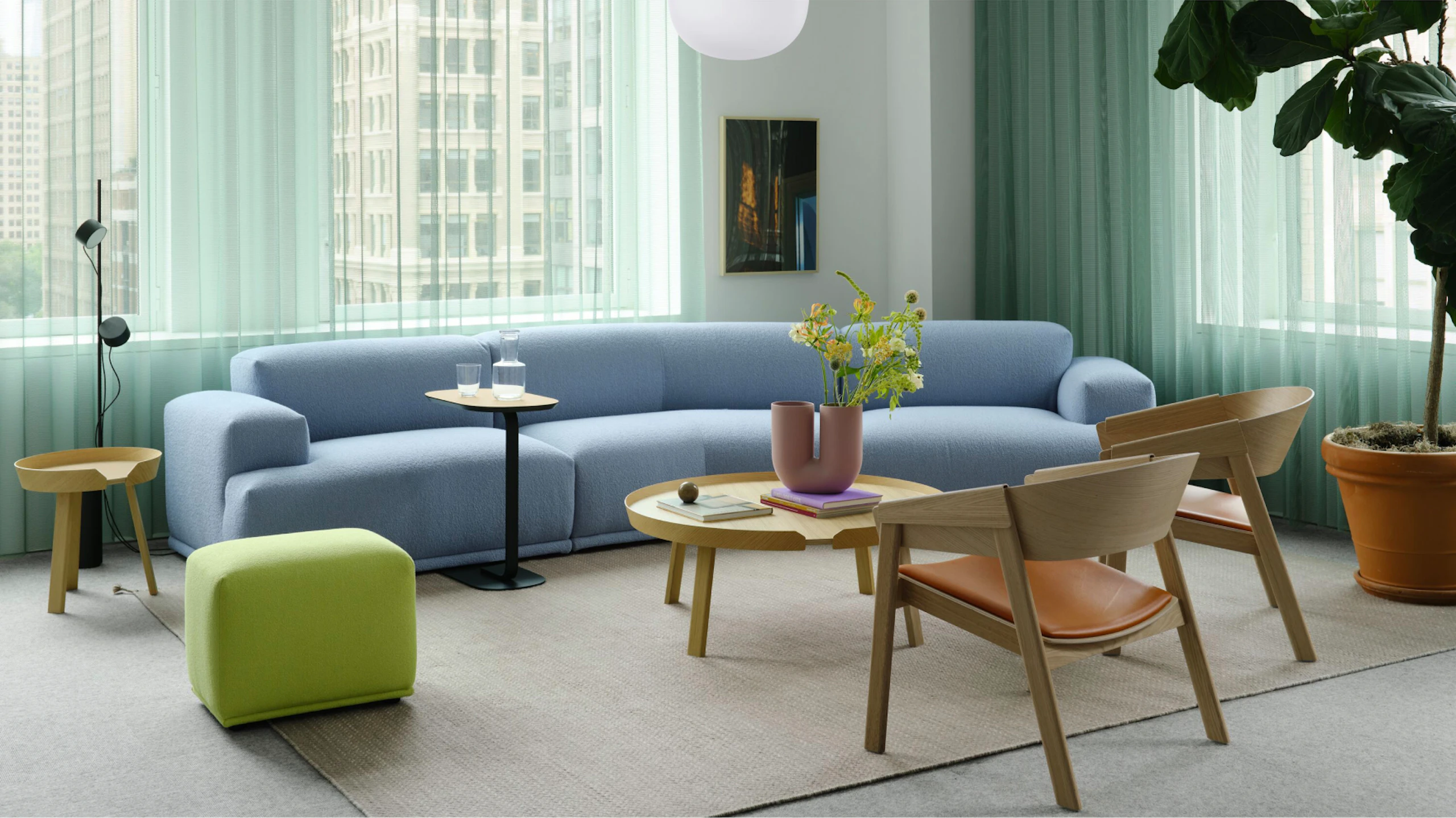 Un sofá azul claro de Muuto, dos sillas y un puf dispuestos alrededor de una mesa de café redonda en el showroom de Muuto en 251 Park Avenue South en la ciudad de Nueva York