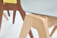 A close-up view of the oak base on a gray naughtone Polly Wood Chair.