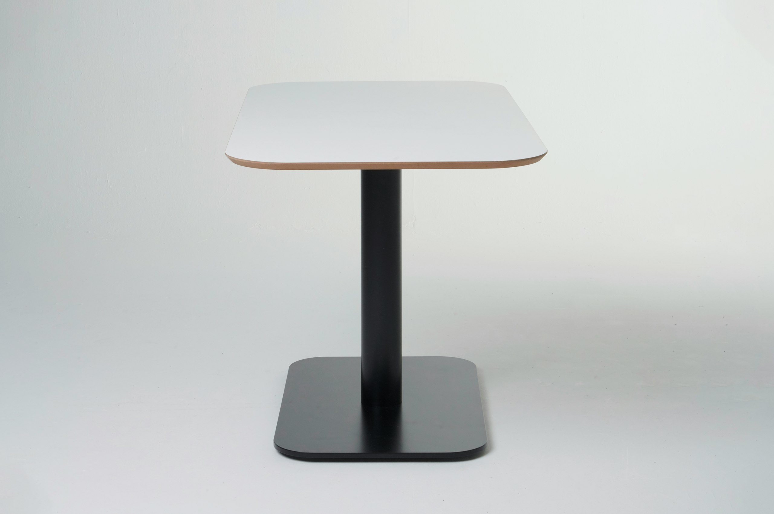 White sweep shot of Hue table with black metal base with white MFMDF table top, viewed from the side.