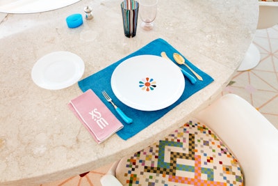 A dining table set with a turquoise placemat, and a white plate with a multi-coloured flower pattern.