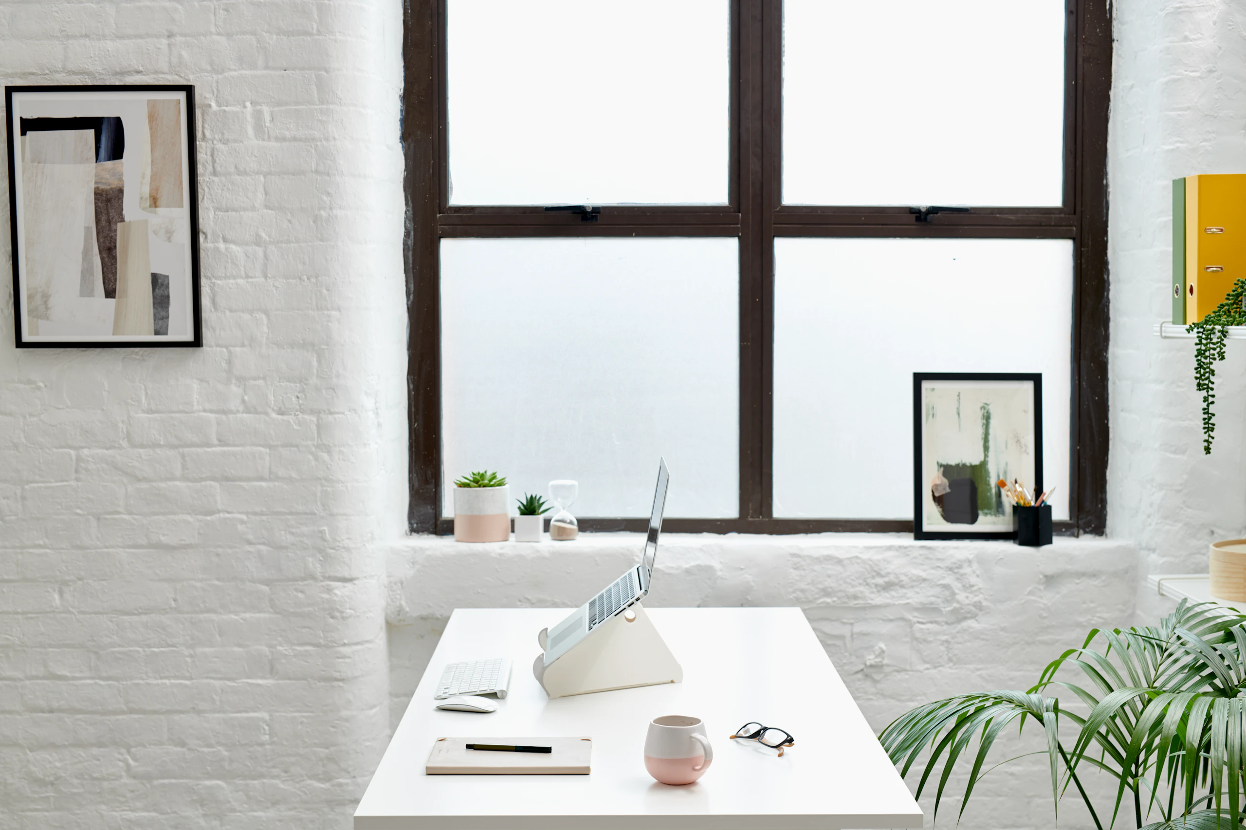 A side view of an Oripura Laptop Stand positioned on a desk in a small office space.