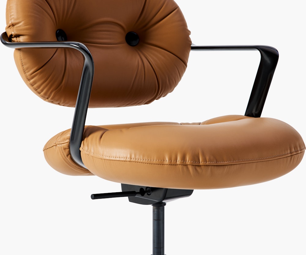 Detail view of a Morrison Hannah chair with a black frame and base with fixed arms and light brown leather upholstery.