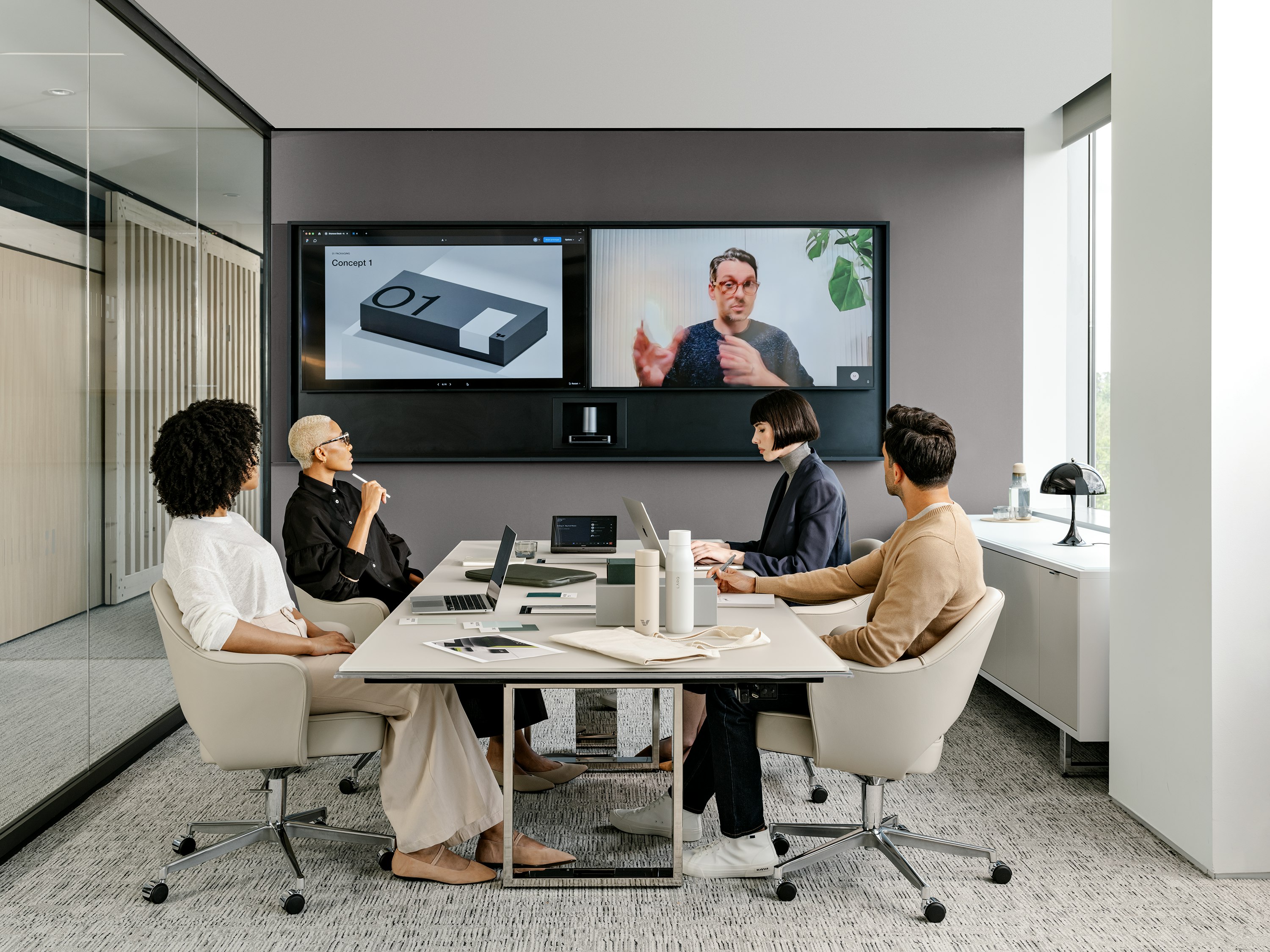 Four people sitting in Knoll Saarinen Executive Chairs at a Highline Conference Table while having a video call with a team member.
