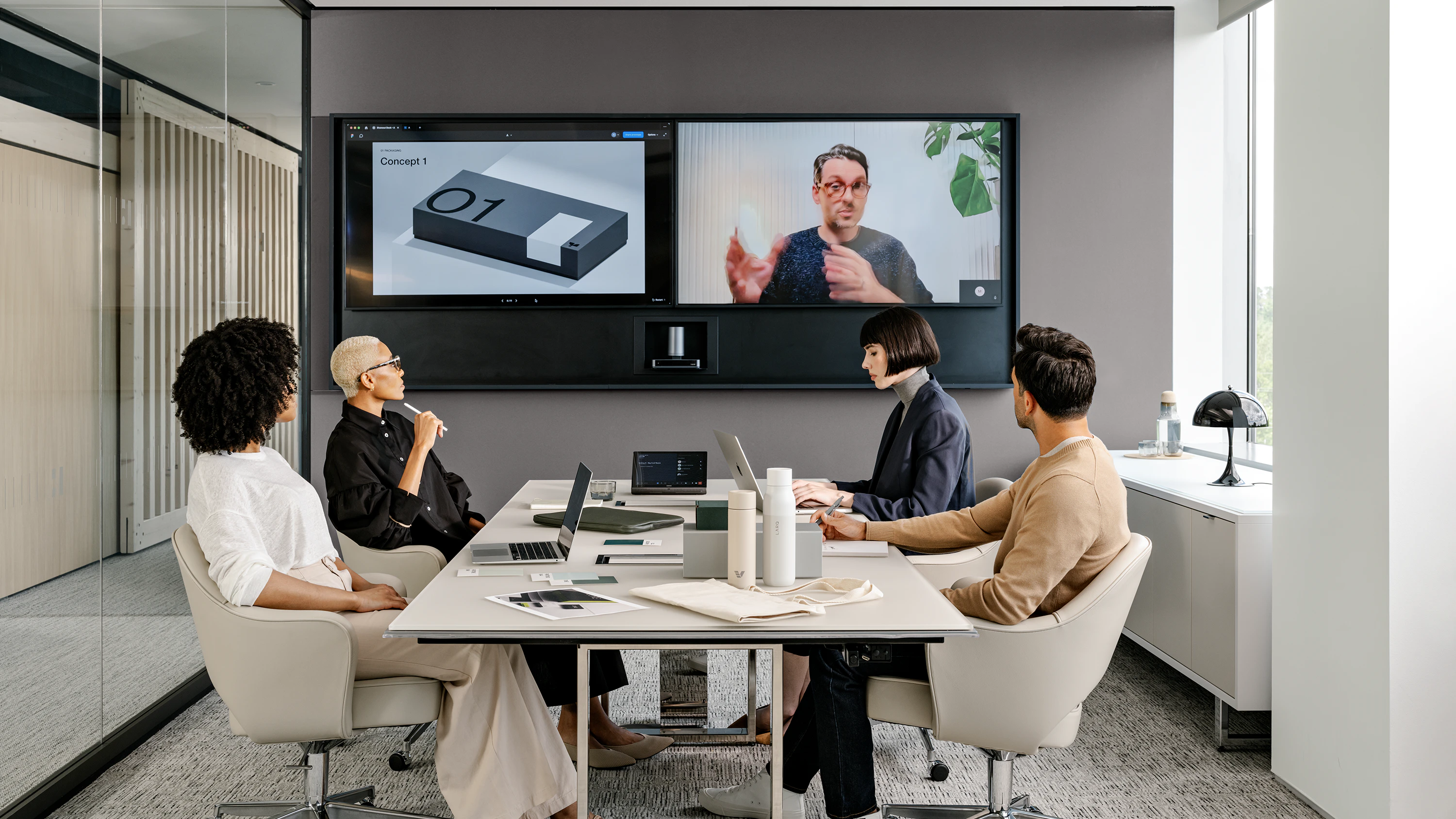Four people sitting in Knoll Saarinen Executive Chairs at a Highline Conference Table while having a video call with a team member.