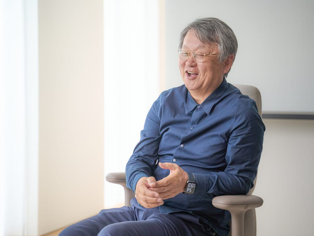 Designer Naoto Fukasawa sitting in a high back Asari chair in light brown.