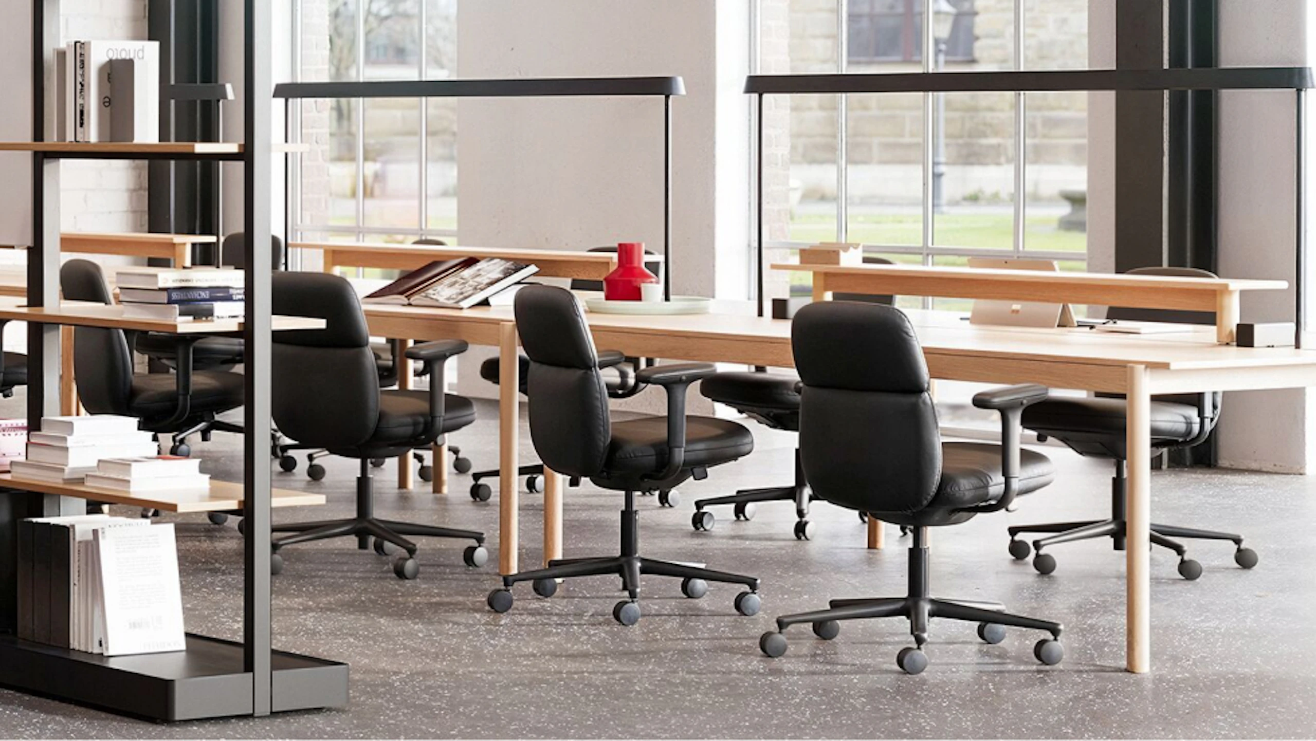 Several black Herman Miller Asari Chairs placed around a Muuto Linear System and Mounted Lamps allowing team members to connect while working individually.