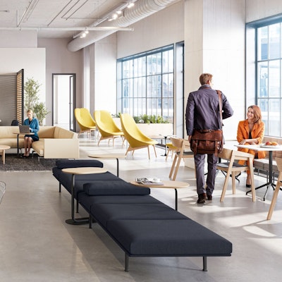 A brightly lit community space featuring three persons utilizing a variety of colorful seating options including the HAY Uchiwa Lounge Chair, Muuto Base Tables, and Muuto Still Cafe Tables