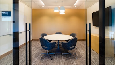 Conference room #425 featuring a Saarinen round table, five grey rolling chairs, see-through glass doors, and a mounted TV on one wall.
