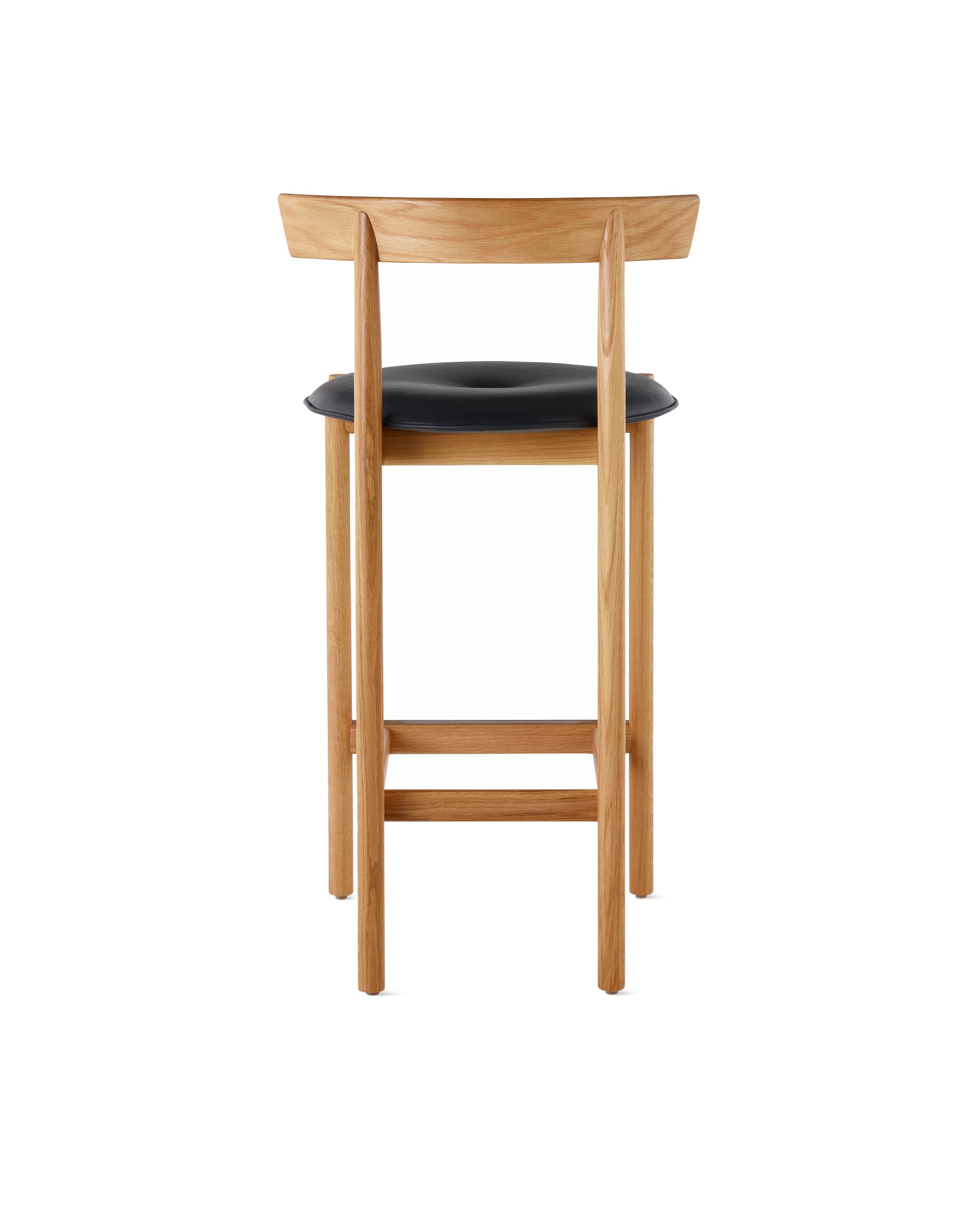 An oak Comma Stool with a seat pad, viewed from the back.