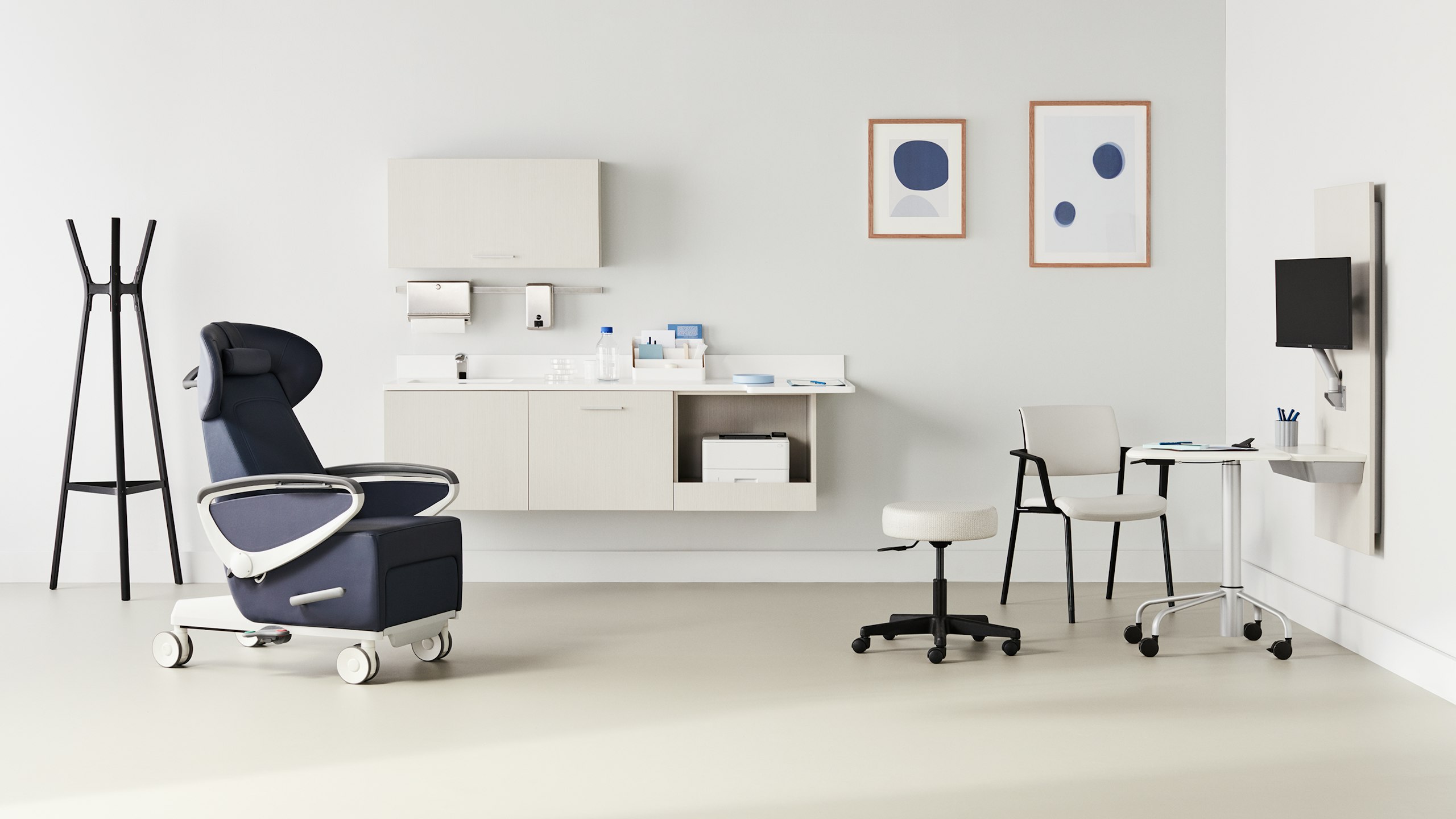 Exam room with a dark blue Ava recliner and an Intent Solution mobile, height-adjustable table and wall unit to the side with a physician stool and Verus side chair in a light gray upholstery and black frame with Mora casework in a light wood laminate on the wall in the background.