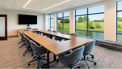 A conference room featuring a large conference table, grey rolling task chairs, and windows overlooking green hills and a pond.