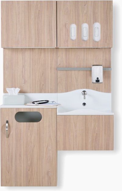 Front view of Compass System casework wall unit in a medium elm wood laminate finish with integrated waste receptacle, white solid surface sink, and upper storage for gloves.