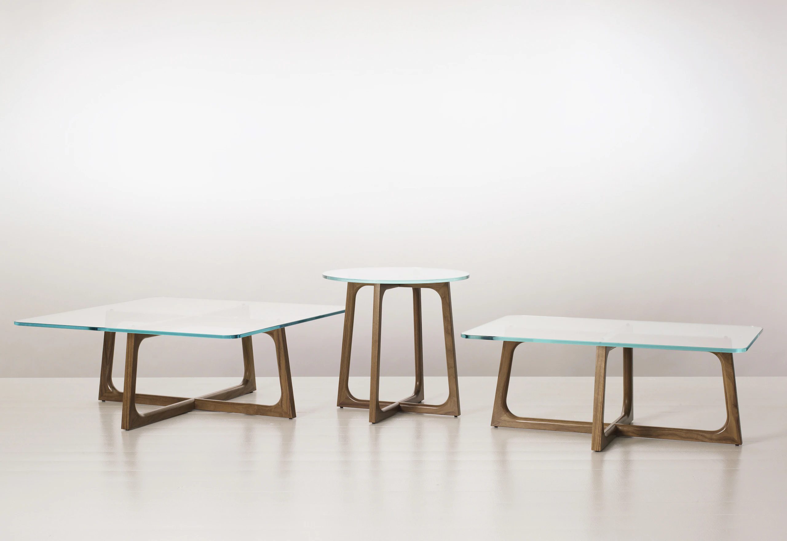 Three Loophole occasional tables of different sizes and shapes, each with a glass top and walnut base.