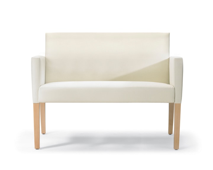 A front view of a Brava 862 plus chair in white textile with upholstered arms and maple legs.